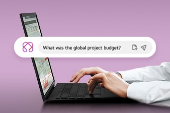 This image shows hands typing on a laptop with a search bar displaying the question, 'What was the global project budget?'