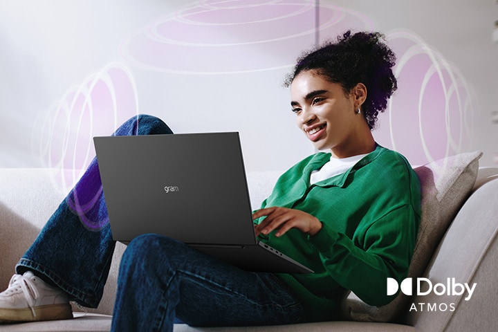 A person sitting on a couch, enjoying immersive audio while using an LG gram laptop. The text highlights Dolby Atmos technology, emphasizing a rich, expansive, 360-degree auditory experience. Surrounding sound waves in the background visually represent the immersive soundscape.	