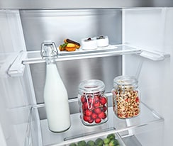 Inside view of an LG refrigerator with a bottle of milk, jars of cherries and popcorn, and small dishes on shelves.