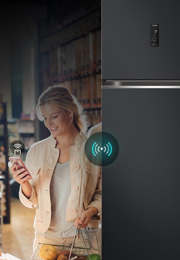 A woman controlling an lg refrigerator remotely using her smartphone. The image highlights the refrigerator's smart connectivity, allowing users to manage and adjust settings from their mobile device.