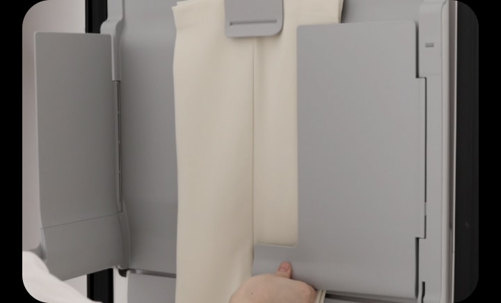 A person using multi-plate EZ Fit PantsPress™ in LG Styler to remove wrinkles and restore pleats to trousers.