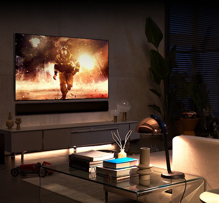 In a spacious and comfortable living room, a TV and soundbar are mounted on the wall. On the TV screen, a firefighter is seen jumping out of a burning building.