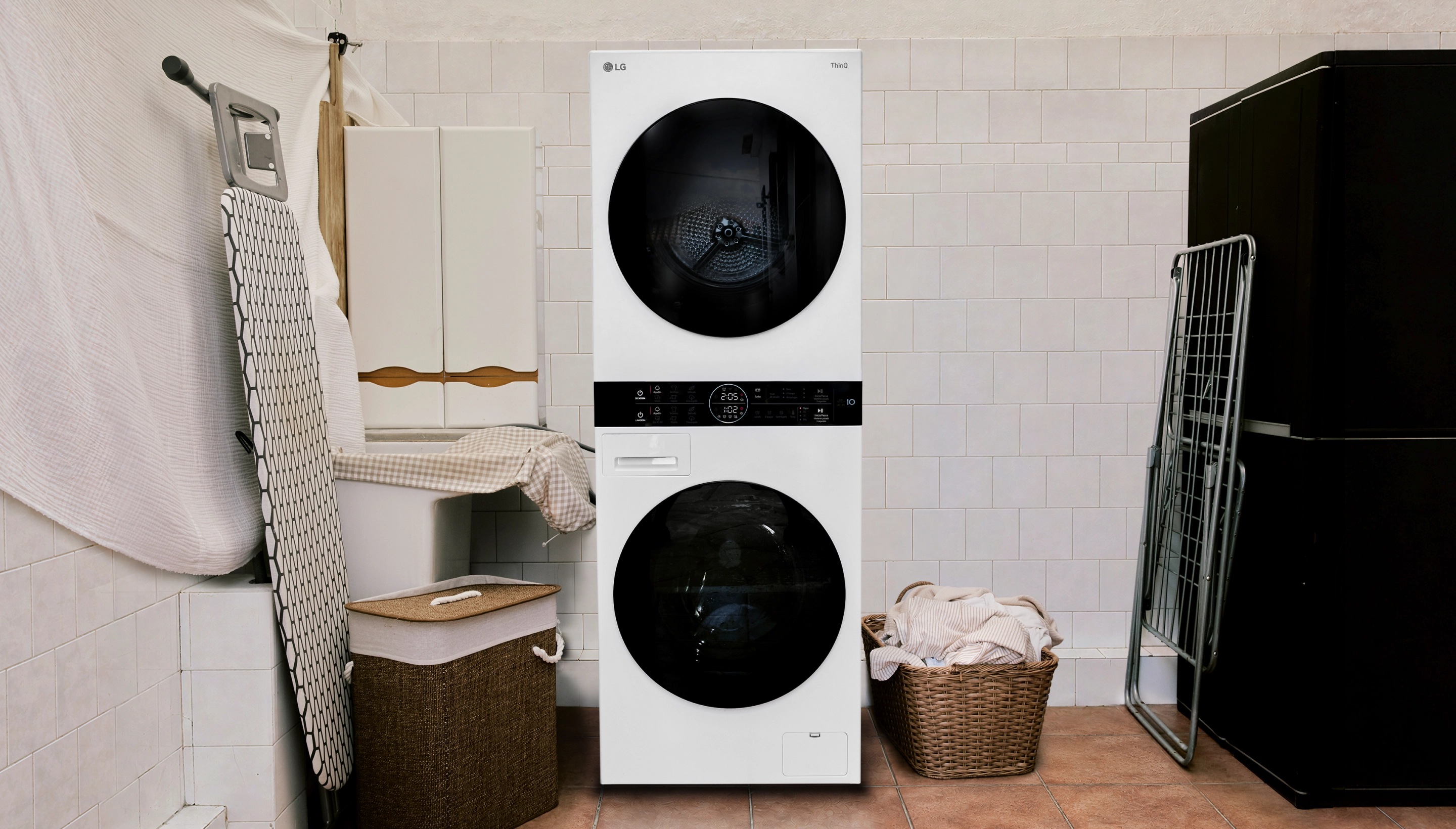 เครื่อง LG WashTower แบบวางซ้อนกันในห้องซักผ้าปูกระเบื้อง ข้างตะกร้าที่เต็มไปด้วยผ้าเช็ดตัว