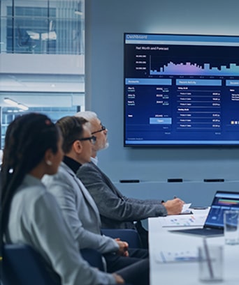 A scene in a company conference room where several people are analyzing performance through a large conference screen connected to a laptop.