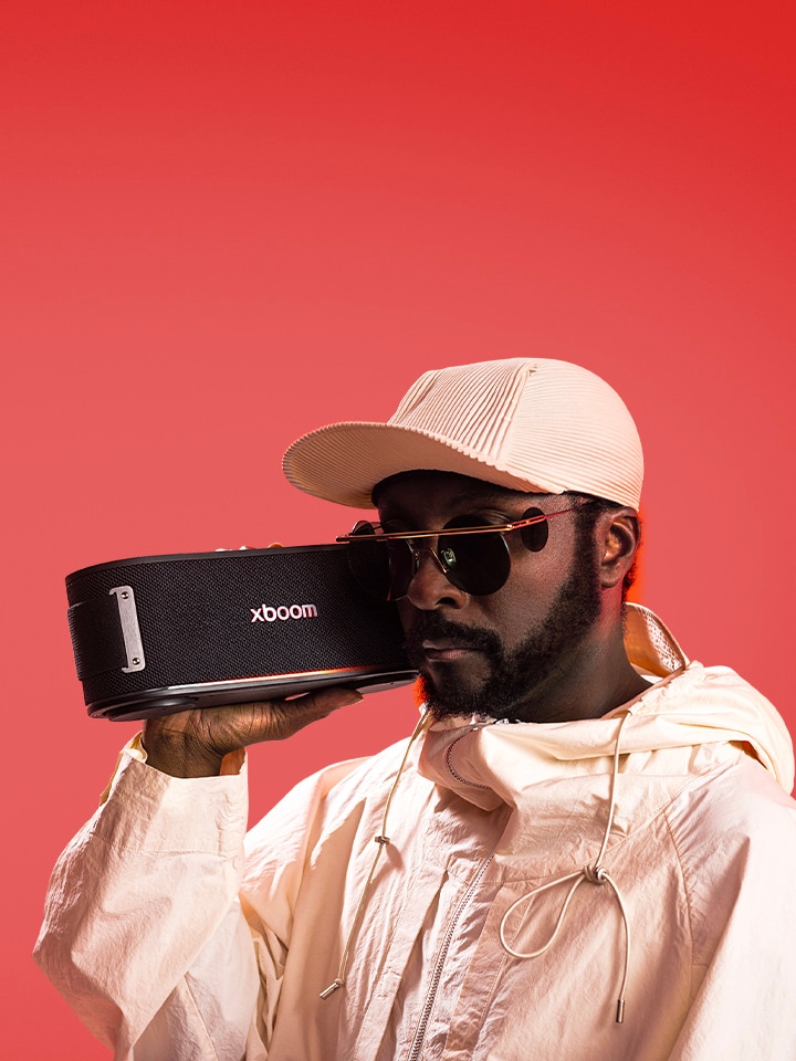 will.i.am ใส่ชุดขาวและแว่นกันแดด กำลังถือ xboom Bounce ใกล้กับใบหน้าของเขา