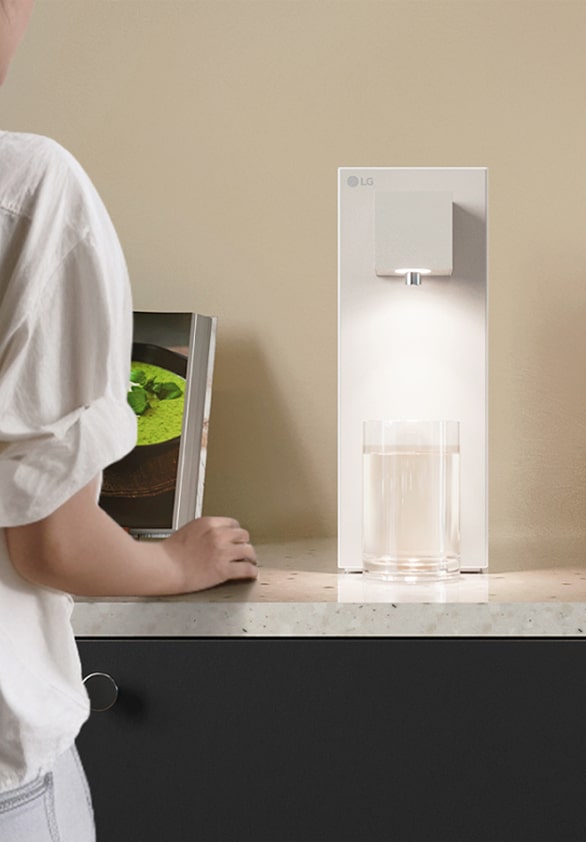 LG water purifier in lifestyle settings with a woman stainding in front of the purifier getting a cup of water.