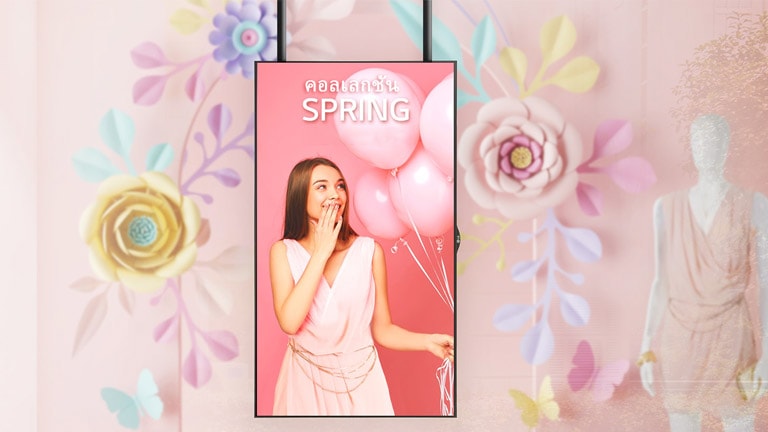 จอแสดงผลที่มีตัวเครื่องแบบบางเฉียบติดตั้งถัดจากหุ่นแสดงแบบในหน้าต่างร้านค้ากำลังแสดงเนื้อหาโฆษณาส่งเสริมการขายให้กับลูกค้าอย่างชัดเจน