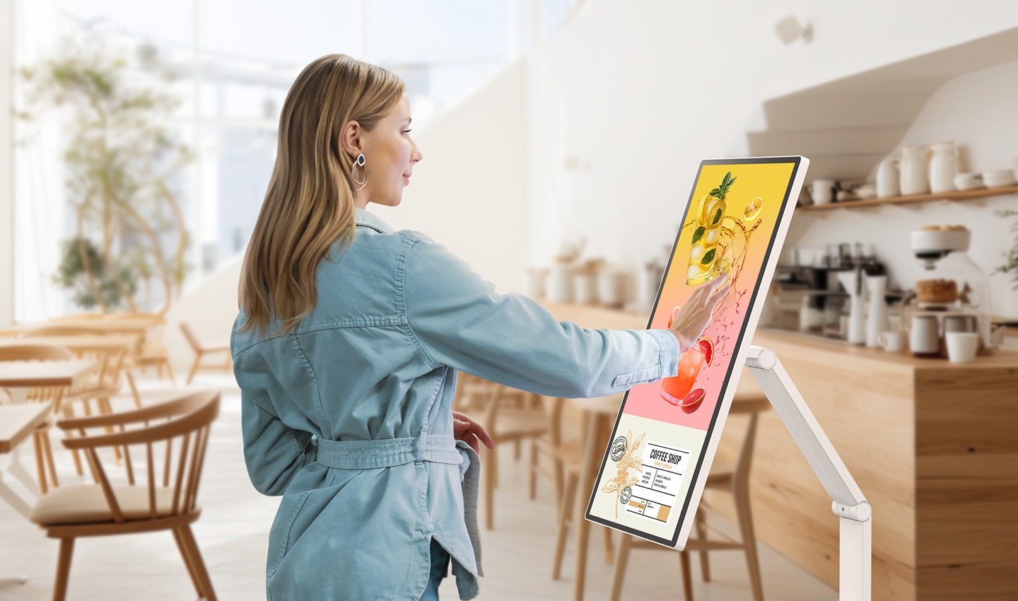ผู้หญิงคนหนึ่งกำลังดูแบนเนอร์กิจกรรมที่แสดงบน LG Smart Monitor Swing ในร้านกาแฟ 