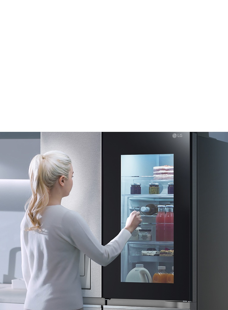 หญิงสาวผมบลอนด์ใช้มือแตะตู้เย็น LG สีดำในห้องครัวทันสมัยที่มีอ่างล้างจาน