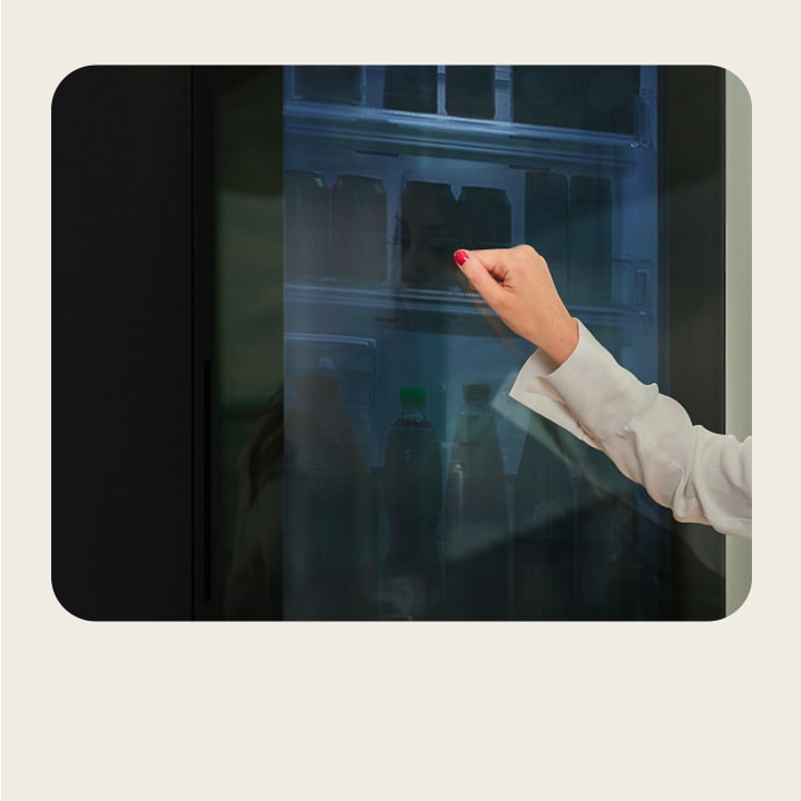 ผู้หญิงคนหนึ่งเคาะที่ประตูกระจกของตู้เย็น LG InstaView แบบอเมริกัน เพื่อดูภายในตู้เย็น	