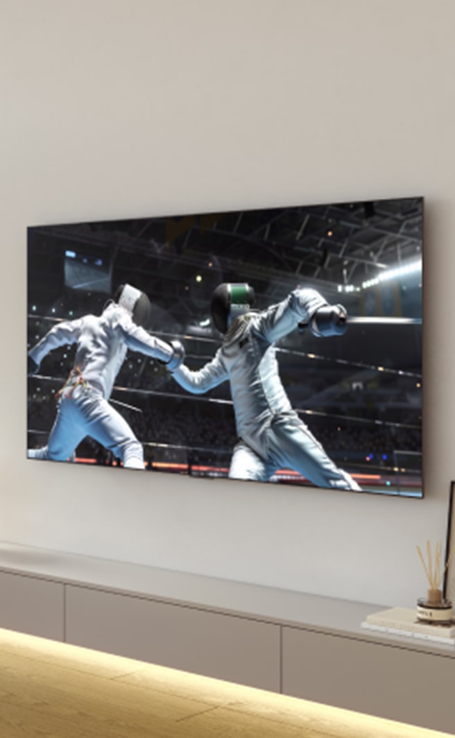 ผู้หญิงคนหนึ่งกำลังชมการแข่งขันกีฬาบนทีวี LG OLED ในห้องนั่งเล่น พร้อมถือแก้วม็อกเทลไว้ในมือ โดยมีตู้เย็น LG InstaView วางอยู่ข้างผนังที่ติดตั้งทีวี	