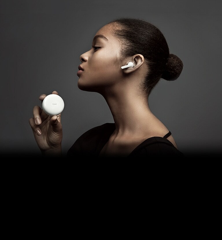 มุมมองด้านข้างของผู้หญิงที่กำลังถือ LG TONE Free ตัดกับพื้นหลังมืด ๆ