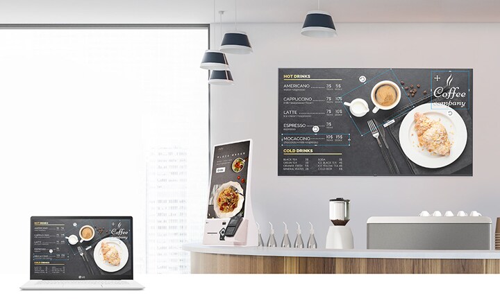 The café's menu board content is being designed using a laptop. Once created, this menu board content is distributed and presented on the signage installed within the cafe.	