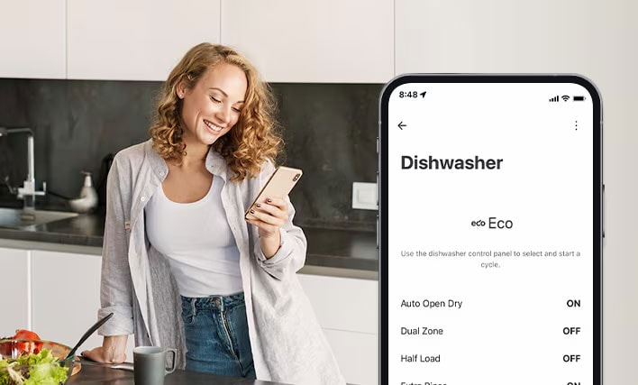 A woman is setting cleaning cycle preferences using the LG ThinQ app in the kitchen.