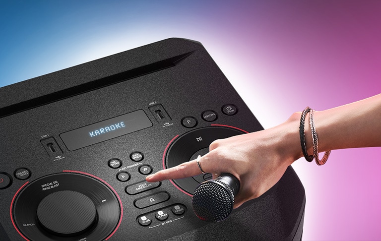 LG XBOOM'un üstündeki Voice Canceller düğmesine basmaya çalışan, mikrofon tutan el.