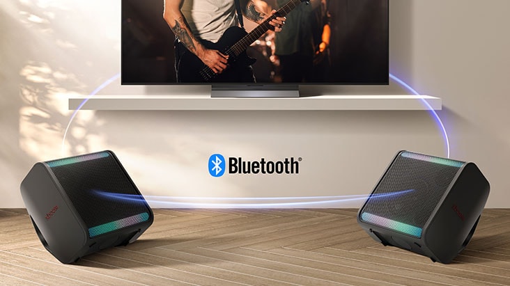 OLED C5 TV is on the wall showing concert scene and two units of xboom Stage 301 are placed on both side of the floor. Virtual blue light streak is connecting all 3 of them to show they're connected via bluetooth.