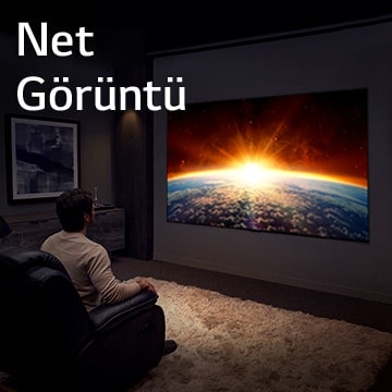 Dünyanın arkasından yükselen güneşin görüntülendiği TV'yi izleyerek karanlık odada kanepede oturan adam.