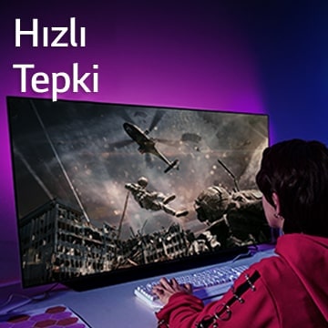 Bir kız, helikopterden inen bir askerin gösterildiği büyük ekran TV ile bilgisayar oyunu oynuyor.