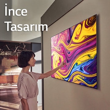 Bir kadın duvarda asılı sanat eserinin sergilendiği bir televizyona bakıyor.
