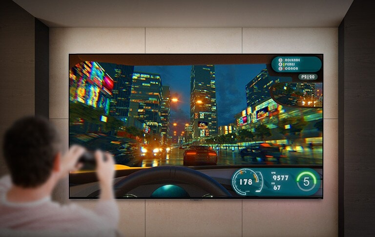 Duvara monte geniş ekran TV'nin önünde oyun kumandası tutan bir adamın arkadan görüntüsü. Ekranda, havadaki bir çarpışmanın ortasında bulunan bir uçağın kokpiti gösterilir.