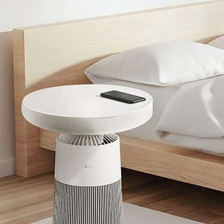 LG Aerospeaker 位於現代風格臥室室內床邊的圖片，頂部放置著智慧型手機，正進行無線充電。	