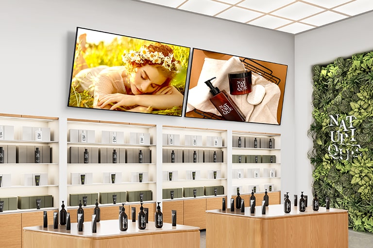 在化妝品商店中，兩台 Signage 顯示器安裝在牆上高處，並向下傾斜，每台顯示器都生動顯示著化妝品廣告。
