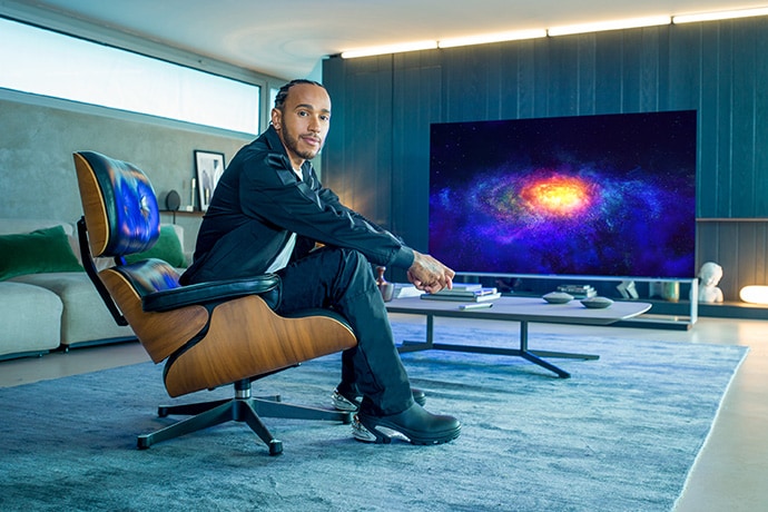 Lewis Hamilton 坐在沙發上，正後方是 LG SIGNATURE OLED 8K 電視