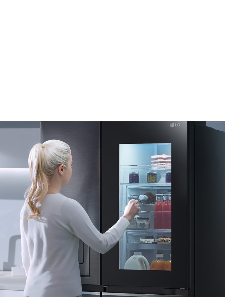 影片顯示,女人走近 InstaView 冰箱並輕敲兩下。冰箱內部燈亮起,不用開門就能看到冰箱裡的東西。視圖放大,聚焦門中的飲料,然後縮小,從後方看到女人正打開門並拿取一杯飲料。