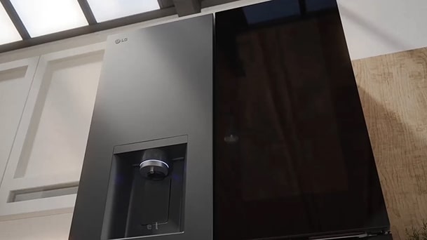 Close-up of black LG InstaView fridge freezer with matte finish. Sunlight from a window above highlights the surface. A built-in water dispenser is on the left side of the door.