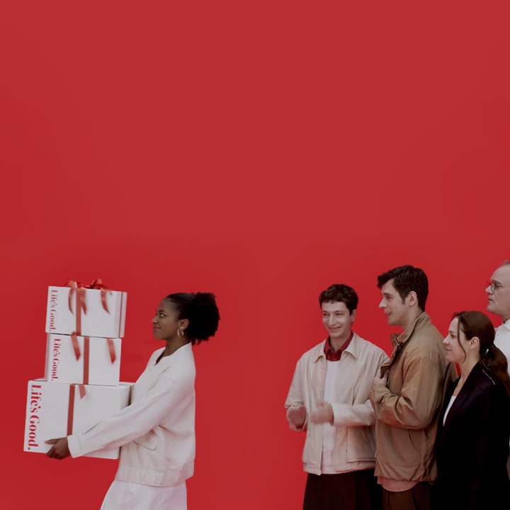 A woman carries several boxes with LG Birthday packaging while people behind her look on with envy.