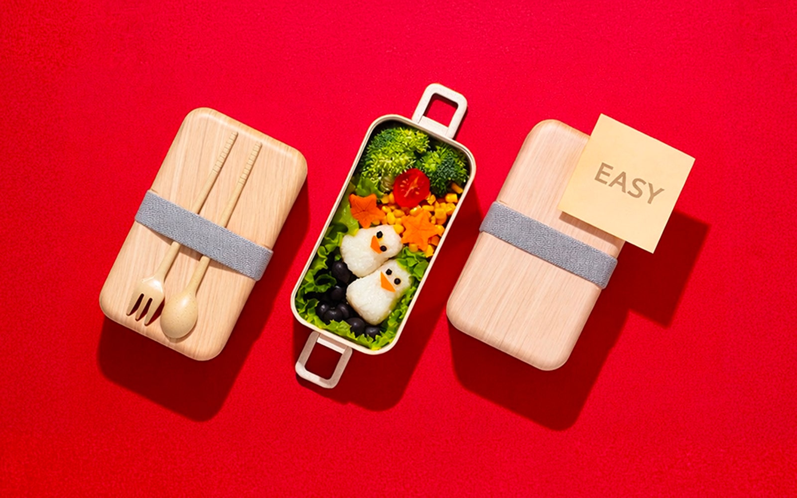 An image showing an easy bento box meal with penguin-shaped rice balls and colorful vegetables on a red background, illustrating a simple meal-prep concept.