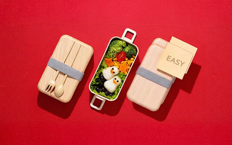 An image showing an easy bento box meal with penguin-shaped rice balls and colorful vegetables on a red background, illustrating a simple meal-prep concept.