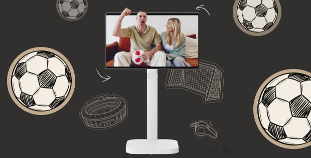 On the screen of the LG Smart Monitor Swing, a couple is seen on the sofa; the man is holding a plush soccer ball and cheering with a raised fist, while the woman smiles next to him.