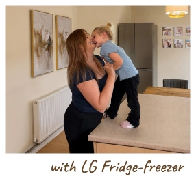 A mother holds her baby in a modern kitchen, standing beside an open refrigerator. [with LG Fridge-freezer]