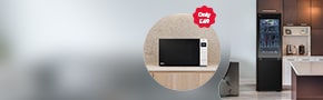 LG Microwave on a light pedestal with two black lg fridge freezers to the right with a light projecting at the centre of the background., inclusive of a promotional message to purchase a microwave at £49 and free delivery