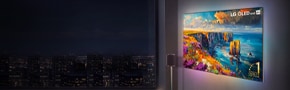 LG OLED evo AI wireless OLED TV wall-mounted in a modern living room, displaying a vibrant coastal landscape with colourful cliffs and ocean views at night.