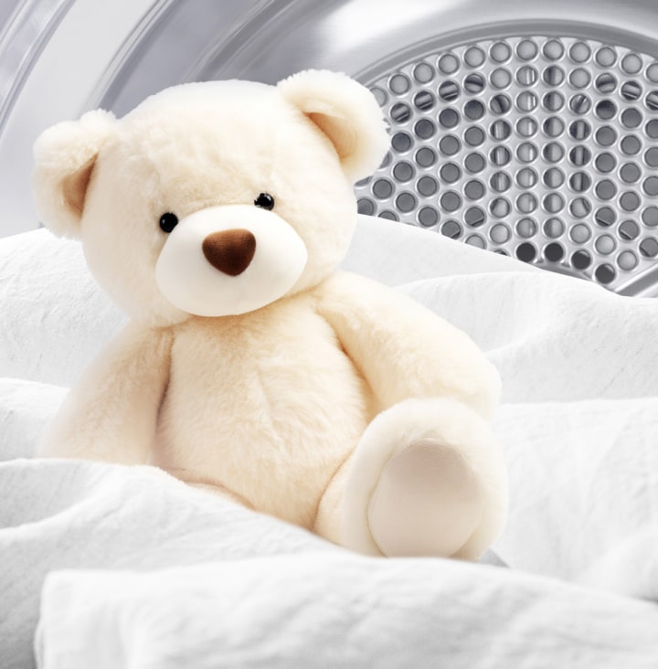 Image of a clean teddy bear and white fabric inside a dryer drum.	