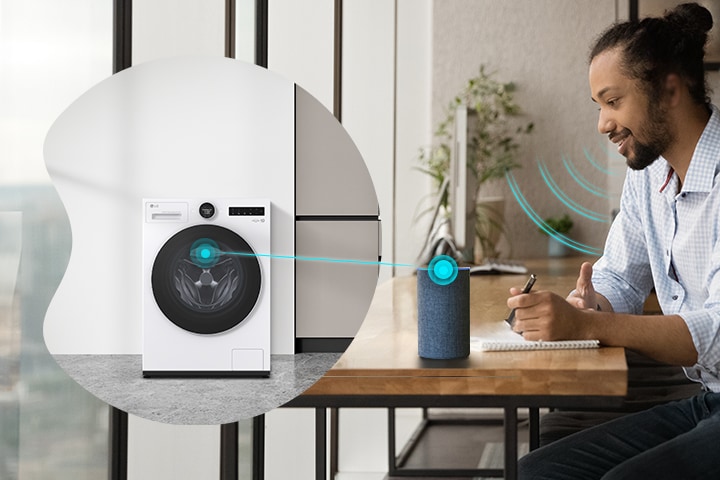 A man sits at a desk speaking through a smart speaker, which is connected by a line to an LG white front load washer dryer on the left, illustrating voice control interaction.