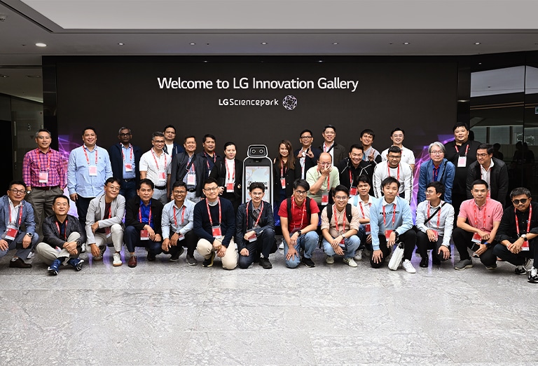 Group of people posing for a photo in front of the  'Welcome to LG Innovation Gallery' sign at LG Science Park.	