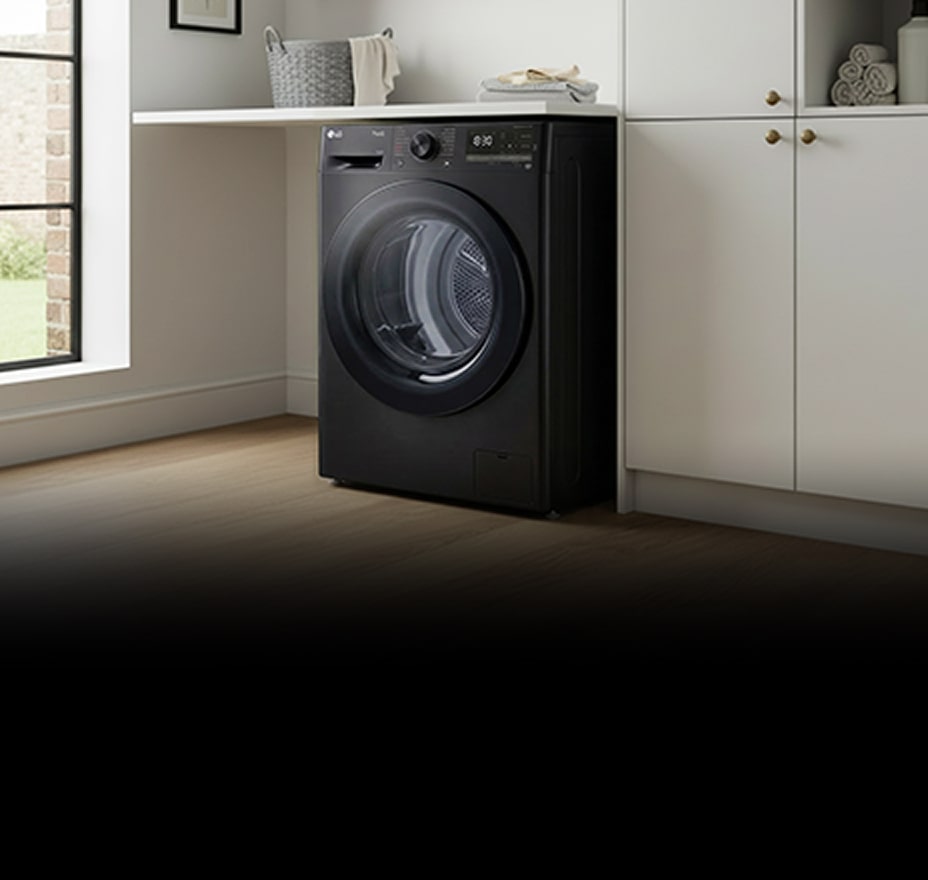 A black front-loading dryer is installed beneath white cabinetry in a bright laundry space.