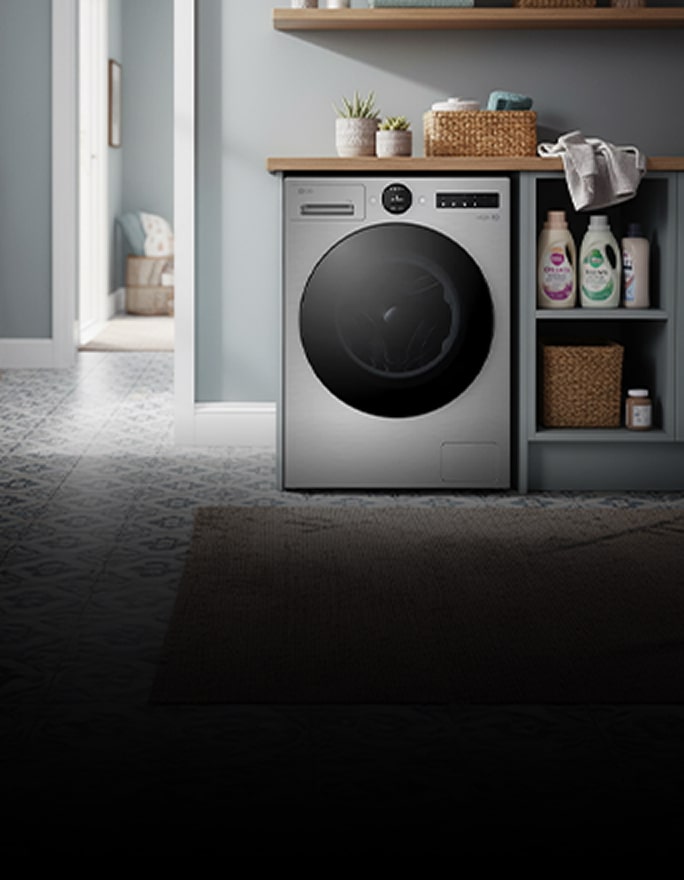 A black front-loading washing machine stands beside wood cabinets, with folded towels on a nearby rack.