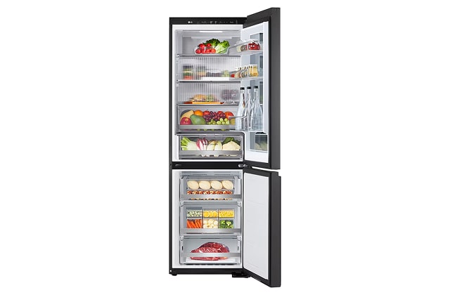A tall refrigerator with the fridge on top and freezer below, opened to show food items and bottled drinks arranged on shelves and in drawers.