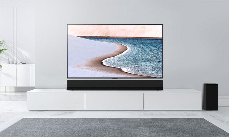 A TV is mounted on light gray wall. LG Soundbar is below it on a white cabinet. The TV shows a beach.