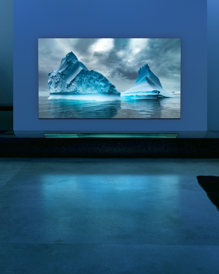 A blue neon circuit moves around on blue glacier image. The camera zooms out and shows this blue glacier within TV screen. The TV is placed in a wide living room with blue background.