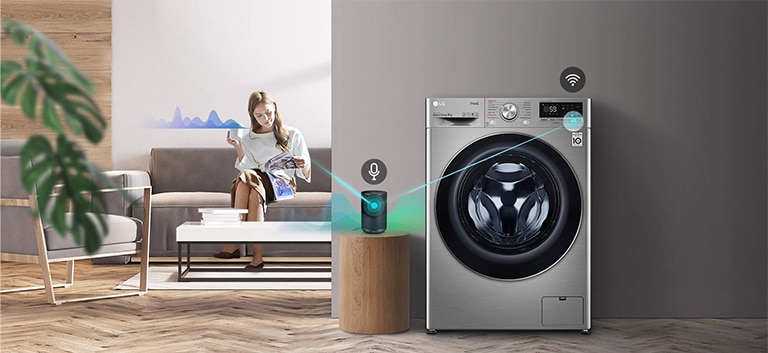 A woman sitting on the couch and drinking tea is giving orders to her washing machine through her AI speaker.