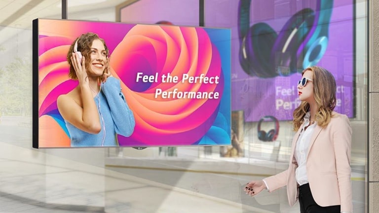 A woman wearing sunglasses is watching ads on the display installed in a shop window, and the ads on the display are very visible even under the strong sunlight.