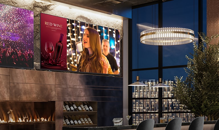 Two displays are installed in the luxurious wine bar. One shows a concert scene, and the other displays two images in one screen showing both a red wine commercial advertisement and a female singer singing.