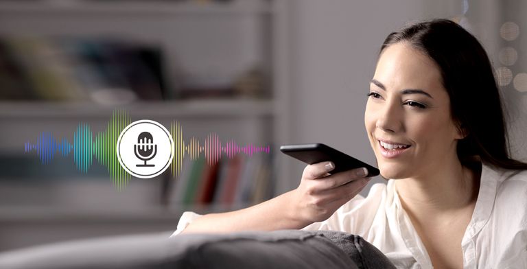 A woman is controlling TV by speaking to a remote control which has voice recognition.