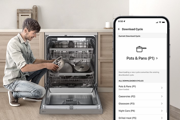 Man loading pots into a dishwasher while using a smartphone to download a washing cycle in a modern kitchen.