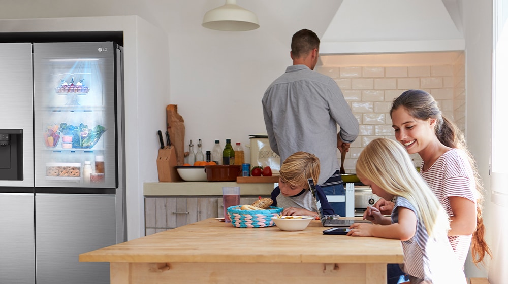 The whole family is sitting at the table preparing a meal. InstaView refrigerator installed on one side of the kitchen is creating cool air quickly.